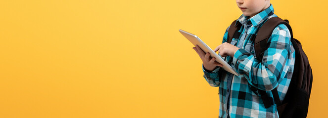 Ginger kid schooler using digital tablet for education, doing homework on yellow studio background,...