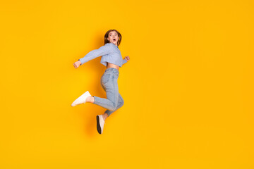 Energetic young woman in casual fashion jumping with joy against a vibrant yellow background showcasing stylish self-expression