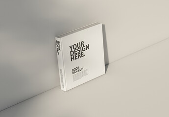 Square book mockup standing on table with shadows on the wall