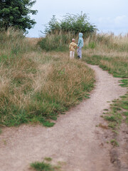 Two children stand together on a dirt path winding through tall grass, facing away under an...
