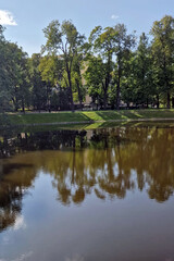 A tranquil park path with lampposts, bordered by lush lawns, under a mix of blue sky and fluffy white clouds.