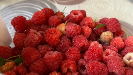 Ripe red raspberries placed in a white bowl, showcasing their natural texture, vibrant color, and...