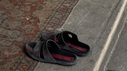 Two black slip-on shoes placed at the entrance of a home, resting on patterned concrete tiles in...