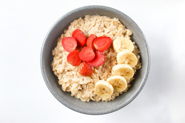 a bowl of oatmeal porridge with strawberries and bananas on top, isolated on a white background