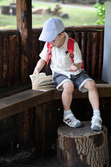 happy little boy in cap sits in gazebo and reads book in summer