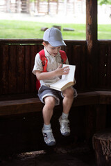 happy little boy in cap sits in gazebo and reads book in summer