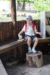 happy little boy in cap sits in gazebo and reads book in summer