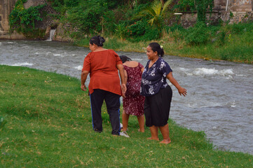 Fototapeta premium The girl stands successfully on the grassy riverbank, joined by the two women who helped her up, walking away together from the stream.