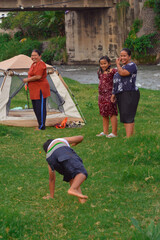 A young boy performs another flip on the grassy area beside the riverside tent, drawing more...