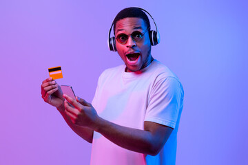 Easy Payments. Excited african american man in white t-shirt and wireless headphones holding...