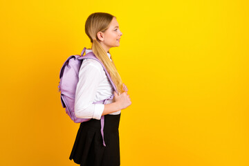 Portrait of a cheerful young schoolgirl with a purple backpack against a vibrant yellow background...