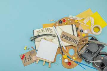 Flat lay of press badge, vintage camera, art supplies, notebook, and exhibition label