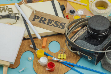 Flat lay of press badge, vintage camera, art supplies, notebook, and exhibition label