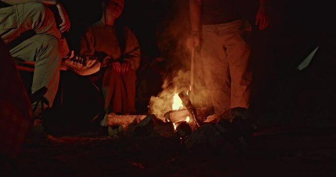 Friends gather around a campfire at night, enjoying the warmth and sharing stories under the stars.