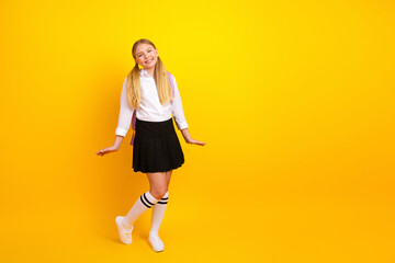 Happy schoolgirl in uniform on yellow background expressing joy and enthusiasm for education and...