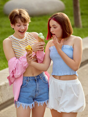 Two friends, gen z, enjoy ice cream treats on a sunny day in a vibrant park. Concept of friendship and joyful outdoor moments.