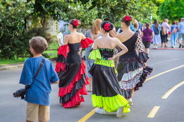 Folk ethnic flamenco dancers walking along street with people. Group of flamenco women dancers in bright dresses walking among crowd at cultural festival in park setting. Spanish Culture Festival