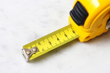 Yellow tape measure on white background. Construction tool for measuring. Close up of plastic housing and metal tape. DIY equipment for building, renovation or home improvement projects.