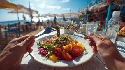 First-person view of hands holding a fork and knife about to eat a colorful meal at an outdoor seaside restaurant 