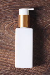 Cosmetic bottle with pump on wooden surface. Blank skincare packaging for branding. White dispenser container for lotion or cream. Natural product mockup for beauty, spa or hygiene design.