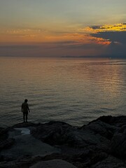 Gentle waves and soft light illuminate the sea at sunset in Thassos, with distant mountains on the horizon.