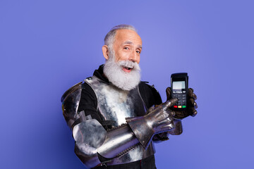 Smiling bearded man in medieval armor holding a payment terminal on a purple background