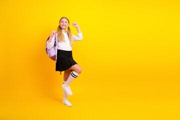 Cheerful schoolgirl posing in uniform against bright yellow background with confident expression...