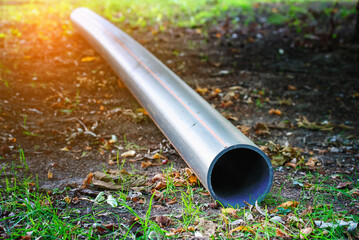 Black plastic hdpe pipe for groundwork to install underground electric conduit system in public park during construction phase. Black hdpe plastic pipes stacked outdoors on ground in grassy park area
