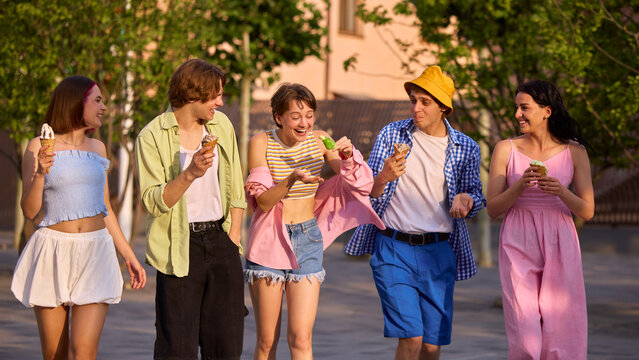 A diverse group of friends enjoys ice cream while strolling through a sunny park. Concept of leisure, friendship, and enjoying life's simple pleasures.