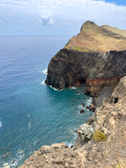 High cliffs on the shore of a small bay on the island of Madeira with a high rocky coastline, huge stones and ocean waves.