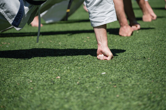 Close-up of karate students doing knuckle push-ups outdoors.
