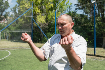 Man in white karate uniform practicing martial arts on a sports field.