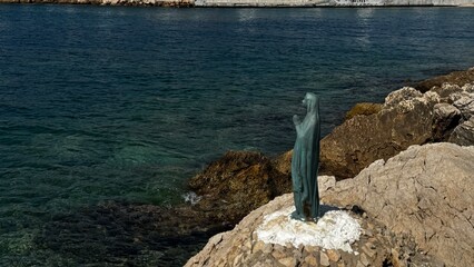 Religious statue of the Virgin Mary placed on a white circular base beside the Aegean coast in Thassos.