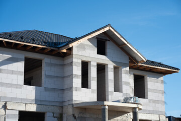 Building under construction with aerated concrete blocks and roof tiles against blue sky,...