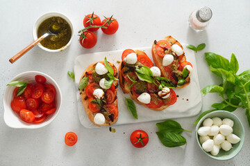Bruschetta with Tomatoes and Mozzarella. Bruschetta with pesto sauce on white board. Mozzarella small ball with basil leaves on white table. Top view.