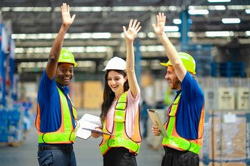 Diverse logistics team in protective gear cheering with hands up, symbolizing goal achievement and...
