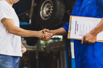 Car service. Mechanic and customer shaking hands. Excellent cooperation between car mechanic and coworker. Close up mechanic and maintenance engineer shaking hands at car workshop.