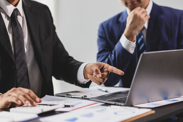 Two businessmen are having a brainstorming session, analyzing financial data on a laptop and...