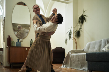 Elderly couple gracefully dancing together in cozy living room setting illuminated by indoor...