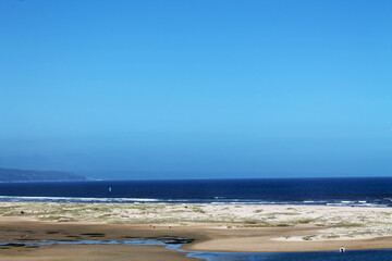 A wide view of a peaceful coastal landscape with golden sand dunes, deep blue sea, and a clear sky. Ideal for travel, nature, or wellness visuals with plenty of copy space.