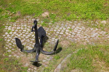 Black anchor on paving stones and green plants