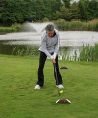 Woman Practicing Golf Swing on a Green Near a Peaceful Pond