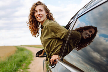 Young woman feeling enjoyment and freedom leaning out of car window. Beautiful woman on road trip...