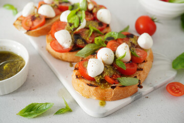 Toasted Bread Bruschetta with Tomatoes and Mozzarella. Bruschetta with pesto sauce on white board. Mozzarella small ball with basil leaves on white table.