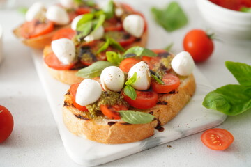 Toasted Bread Bruschetta with Tomatoes and Mozzarella. Bruschetta with pesto sauce on white board. Mozzarella small ball with basil leaves on white table.