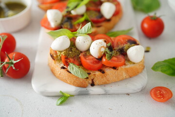 Bruschetta with Tomatoes and Mozzarella. Bruschetta with pesto sauce on white board. Mozzarella small ball with basil leaves on white table.