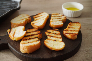 Slices of fresh bread on wooden board with olive oil.