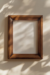 Empty wooden picture frame hanging on a beige wall with leaf shadows