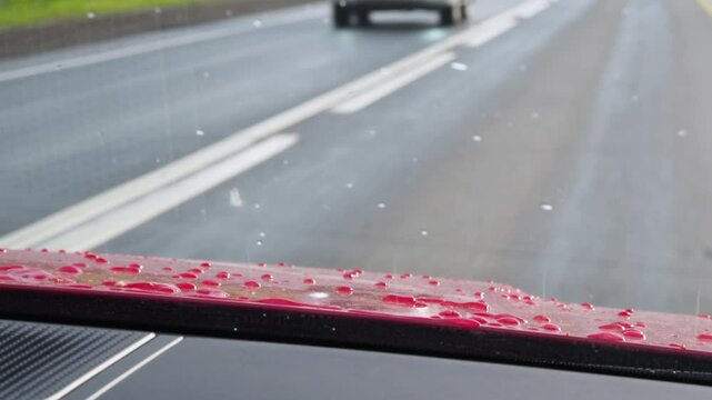 Drive along the highway in a red car. The traffic of the road looking at the hood of the car with drops after the rain. Wet, evening road. Looking at the road through the car window