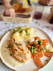 plate with dinner dish, salmon with cream sauce, young potatoes and fresh boiled vegetables, fish dish in a restaurant